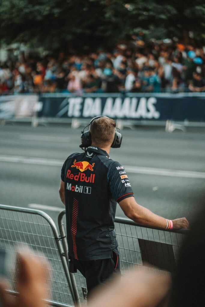 Race official in branded gear observing a formula one event at a stadium with spectators.